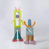 Two toy figures made from colorful solid wood shapes are displayed against a white background. The left figure is taller with green legs and cat-like ears, while the right figure is shorter with orange and blue pieces resembling a person with large, purple shoes—perfect for imaginative free building with the Grimm's Building World Cloud Play Block Set.