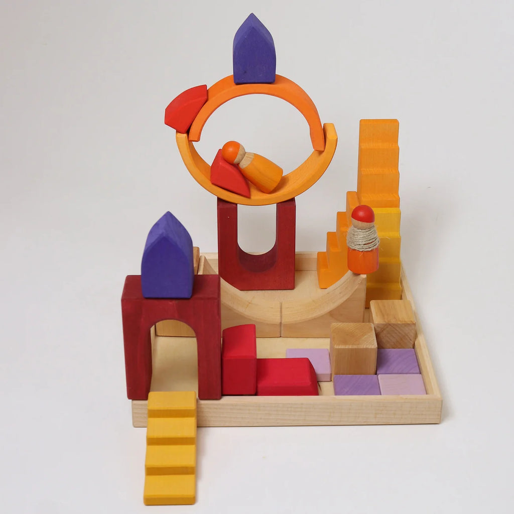Grimm’s Building World - Desert Sand blocks and three small peg dolls are arranged on a wooden tray to create a miniature playground for imaginative free building.