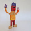 A whimsical figure constructed from Grimm’s Building World - Desert Sand blocks, featuring orange curved arms, a red mouth, and a purple top-knot.