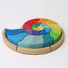 A colorful, curved Grimm’s Building Set Ammonite Shell featuring wooden pieces arranged in a spiral on a circular base as a creative shape puzzle.