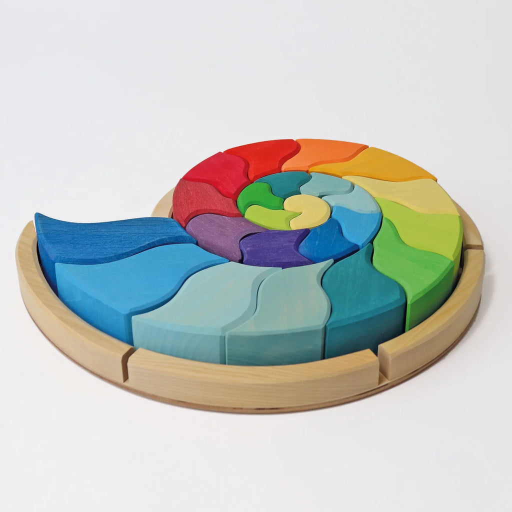 A colorful, curved Grimm’s Building Set Ammonite Shell featuring wooden pieces arranged in a spiral on a circular base as a creative shape puzzle.