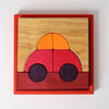 Grimm's Building Set - Red is a vibrant wooden puzzle in a red frame, featuring block pieces that form a simple car with an orange and yellow top, red body, two dark wheels, and a brown base.