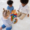 Three young children sit on a white carpet, playing together with the Grimm's Assembly Set Musical Ball Run, assembling the colorful wooden tracks and sending marbles racing down the tower.