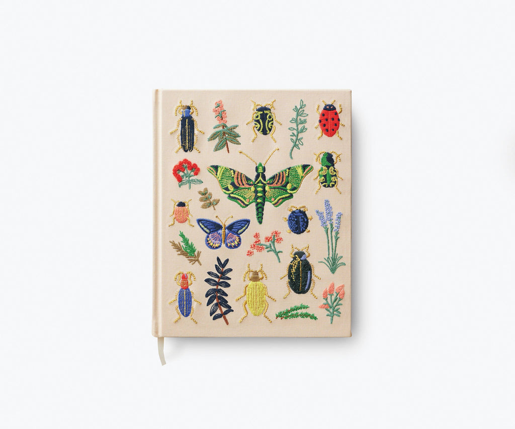 The Curio Embroidered Fabric Sketchbook is a beige hardcover journal featuring colorful embroidered insects—beetles, butterflies, a ladybug—and delicate flowers and leaves, making it the perfect sketchbook for nature lovers.