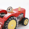 Close-up of the Farmyard Tractor & Trailer, a red wooden farm toy with black and yellow wheels, a circular steering wheel, and painted mechanical details on the side.