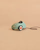 A small, mint green toy car from the Maileg Little Brother Driver Set—with white and red wheels and a black pull string—sits on a plain beige background.