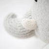Close-up of Cuddle + Kind Evan the Elephant, a hand-knit gray elephant doll with yarn-stitched trunk and tusks. This stuffed animal helps provide meals to children and is photographed against a softly blurred background.