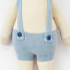 Cuddle + Kind Sebastian the Lamb is a sustainable fair trade hand-knit doll in light blue overalls with suspenders, cream-colored arms, legs, and torso. The doll’s head is not visible in the image.