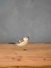 The Hand Carved Ornament - Sparrow Bird - 3.5"H is a small wooden figurine displayed on a wooden surface with a plain gray background.