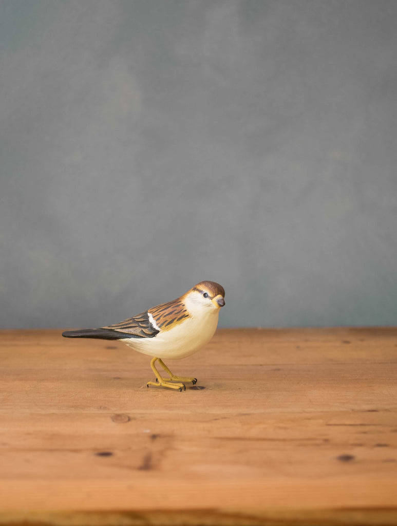 The Hand Carved Ornament - Sparrow Bird - 3.5"H is a small wooden figurine displayed on a wooden surface with a plain gray background.