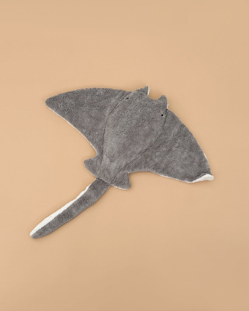 The Senger Naturwelt Stuffed Animal - Large Manta Ray is a sustainably crafted gray plush toy with a long tail and two small black eyes, shown on a plain beige background.