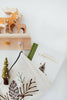 A Christmas stocking with pinecone embroidery hangs on a wooden hook. Nearby, “Our Little Adventure at Christmas (Baby’s First Christmas)” board book peeks out—perfect for toddler language skills and holiday gifting. Above, wooden animal figurines rest on a shelf.