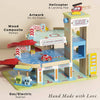 Le Grand Wooden Garage: a handmade playset with ramps, gas/electric station, elevator, floor artwork, red toy car, helicopter with landing pad, and labeled signage—perfect for imaginative play. "Hand Made with Love" at the bottom.