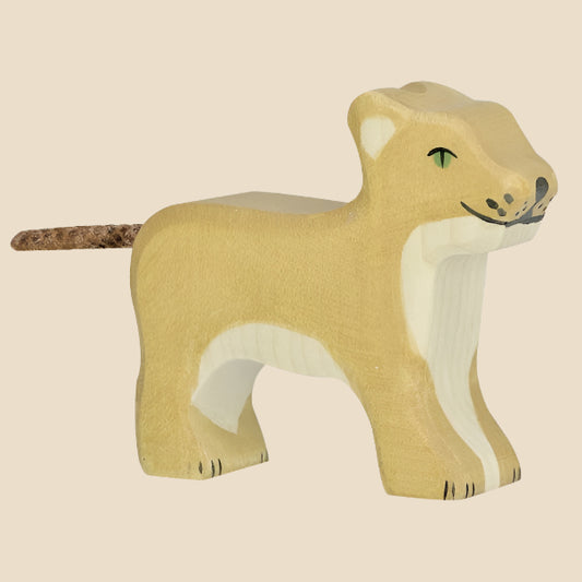 The Holztiger Lion Cub is a handcrafted wooden figure painted light brown with white accents, green eyes, and a cork-like tail. Made in Europe, it stands on all fours and ships in one week.