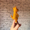 A hand holds a small, handmade orange felt Shiba-Inu Dog Finger Puppet with a tail, viewed from the back against a white brick wall—ideal for wool finger puppet enthusiasts.