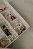 A close-up of a Sabo Concept Christmas Ornaments gift box shows compartments with white shredded paper, filled with hand-painted wooden decorations—a toy soldier, a white rocking horse, and a ballerina Christmas tree ornament.