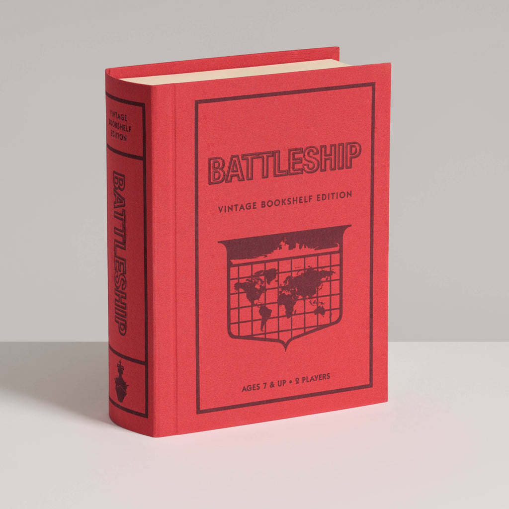 A red hardcover "Board Book: Battleship Vintage Bookshelf Edition" stands upright on a light gray surface, showing a world map and classic strategy game details for 2 players, ages 7+.