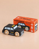 A black cab toy with wooden wheels is placed in front of an orange box labeled “No. 45 GT275 Bertie | Made in England.” The box features images and details about the London toy car.