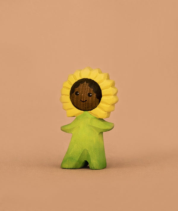 The Bumbu Handmade Wooden Flower Child Sunflower is a small wooden figurine with a smiling face, yellow sunflower headpiece, and green outfit—a charming Waldorf toy for imaginative play. Ships in one week.