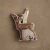 The Coral & Tusk Deer with Lights Ornament is a woodland-inspired deer ornament with embroidered details and a blue bird perched on string lights, hanging by a loop against a beige background—perfect for your Christmas tree.