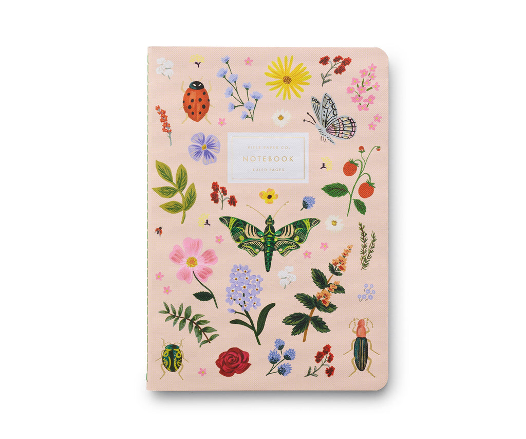 This pale pink ruled notebook features colorful illustrations of flowers, leaves, butterflies, beetles, a ladybug, and cherries. A white label with gold "Notebook" lettering accents the cover. Part of the Assorted Set of 3 Curio Notebooks.