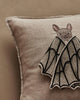 The Coral & Tusk Bat Wing Surprise Pillow is a beige linen cushion featuring an embroidered bat with its face and butterfly-like open wings on a neutral background.
