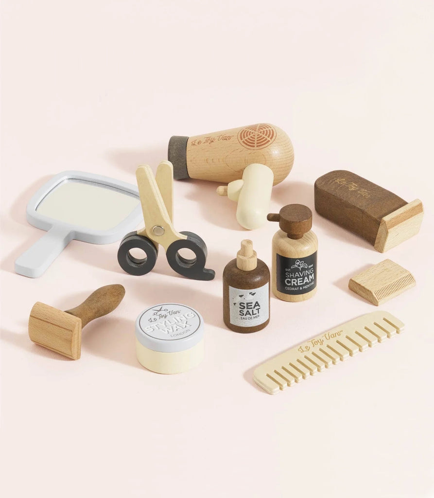 The Wooden Hairdresser & Barber Kit (ships in one week) is a plastic-free wooden toy grooming set—scissors, hair dryer, mirror, comb, brush, bottles, shaving cream, sea salt, soap, clippers—displayed on a light pink background.