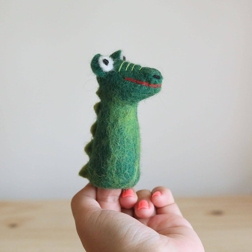A hand holds the Felt Gator Finger Puppet—a green felt crocodile with stitched eyes and a red smiling mouth—ideal for imaginative play or storytelling, shown against a plain light background.