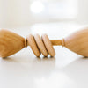 Two Wooden Baby Rattles, made in USA, touching fingertips in a soft, minimalist setting with a bright, blurred background.