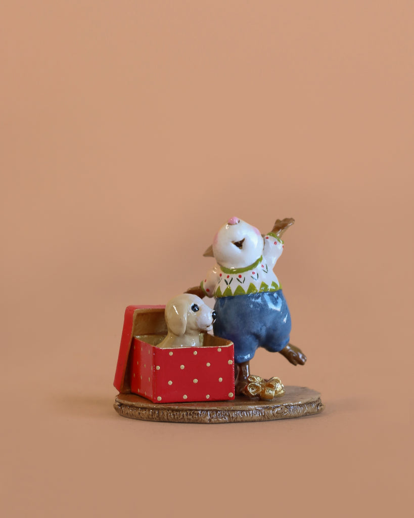 The Wee Forest Folk Tiny Collectible - Christmas Critter features a hand sculpted mouse in blue overalls next to a red polka dot gift box with a puppy inside—a charming piece for any miniatures or Wee Forest Folk collection.