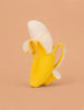 The Ana Banana Teether features a banana with its peel partially open, but the fruit is replaced by a white ceramic coffee cup on a solid light brown background, creating a whimsical sensory play toy.
