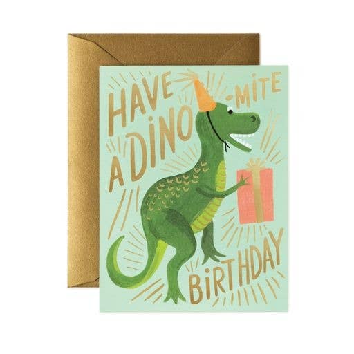 The Dino-mite Birthday Card shows a green dinosaur in a party hat with a gift and playful "Have a DINO-mite Birthday" lettering. It includes a metallic gold envelope and has a blank interior for your personal message.