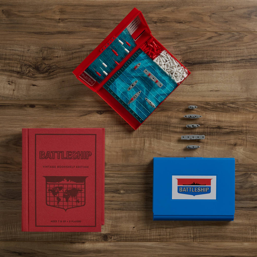 Board Game: Battleship Vintage Bookshelf Edition is a naval action game with a wooden playing surface, an open red box holding ships and pegs, a red hardcover rulebook, and a closed blue box featuring the Battleship logo.
