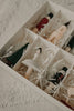 The Sabo Concept Christmas Ornaments come in a box with shredded paper and separate compartments, featuring hand-painted wooden pieces shaped like a ballerina, Christmas tree, nutcracker soldiers, and a house.
