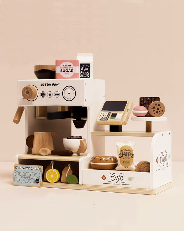 The Barista Café Shop, shipping in one week, is a wooden tabletop playset with a pretend espresso machine, cash register, loyalty card, plus play food such as chips, cookies, donut, lemon slices, and milk on a cream background.