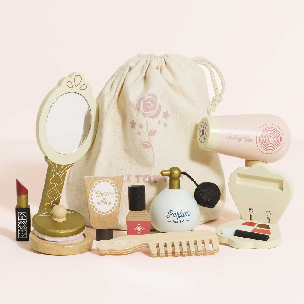 The Vanity Star Beauty Kit is a charming wooden makeup toy set for imaginative play, featuring a mirror, hair dryer, lipstick, and more—all neatly arranged before a beige drawstring bag with a rose design.
