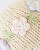 Close-up of Cuddle + Kind Tiny Emma the Mouse: a cream-colored, handknit fabric made in Peru, features embroidered light pink and lavender floral designs with green leaves.