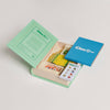 Open box Clue Jr. Vintage Bookshelf Edition set with a blue instruction booklet, a card showing game characters, a folded yellow game board, and four character tokens in a molded tray.