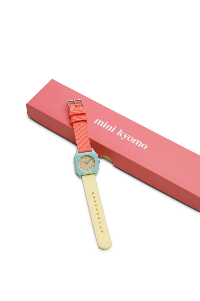 The Mini Kyomo Watch - Bubble Gum, featuring a coral and yellow strap, is shown next to a pink box labeled “mini kyomo” on a white background.