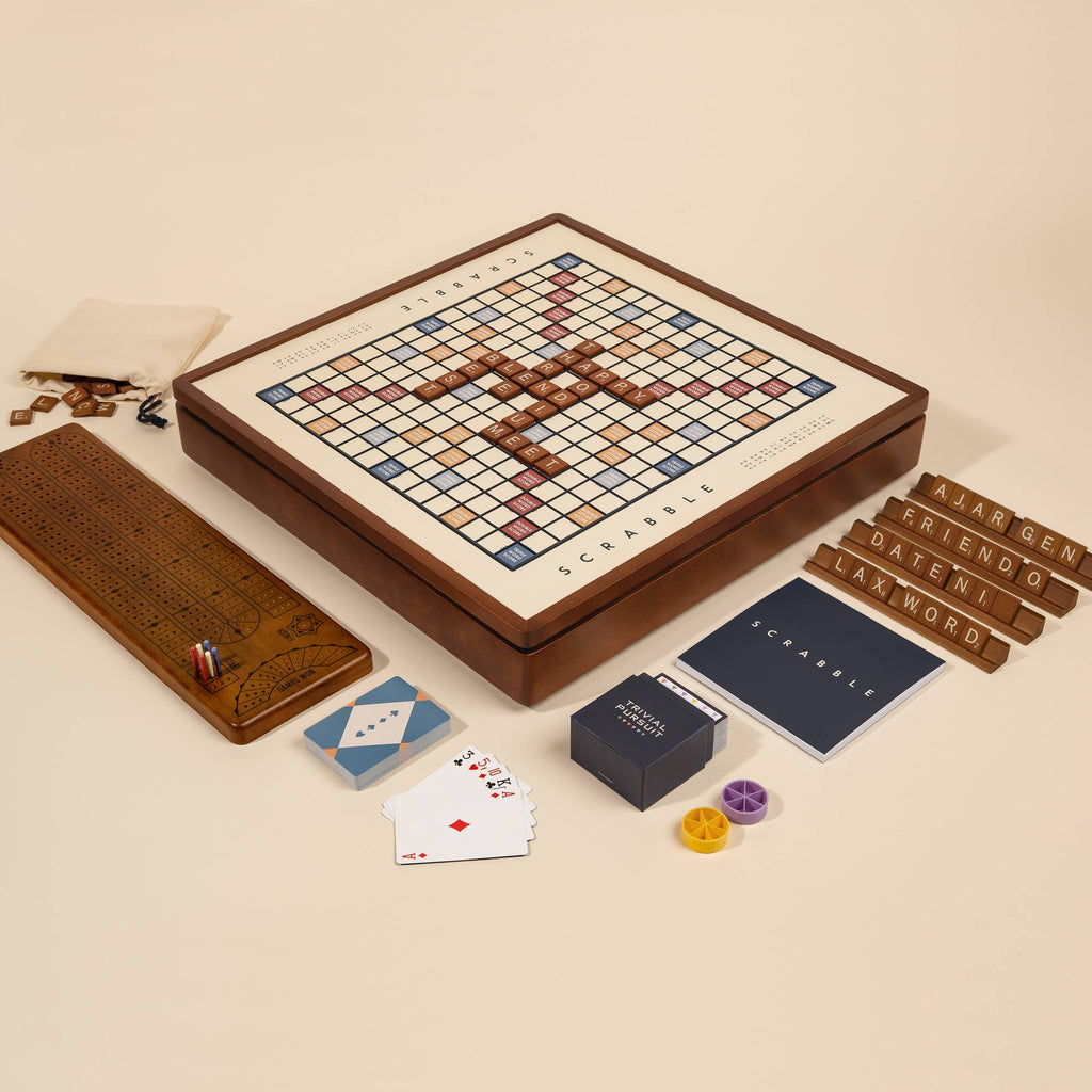 The 3-in-1 Game Collection: Scrabble, Trivial Pursuit & Cribbage includes a wooden Scrabble board with tiles and racks ("LARGEN," "FRIENDO"), a scorepad, Trivial Pursuit cards, Cribbage board, and accessories on a beige background.
