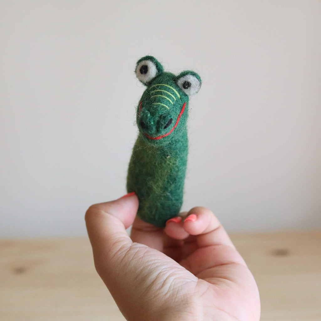 A hand holds the Felt Gator Finger Puppet, shaped like a crocodile with big round eyes and a red stitched smile—perfect for imaginative play or storytelling—against a light background.