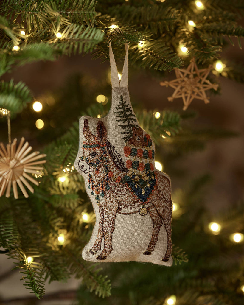 A Coral & Tusk Christmas Donkey Ornament featuring an embroidered donkey hanging on a Christmas tree, with a pack carrying a tree and a small bear.