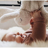 A smiling baby in a pink knitted sweater lies on a soft, fluffy surface, playing with a large Senger Naturwelt Cuddly Animal - White Bunny.