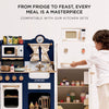 A young child plays with the Wooden Microwave, a sustainable wood play kitchen set. The navy oven, stove, white refrigerator, and accessories inspire imagination. Text above: "From fridge to feast, every meal is a masterpiece." Ships in one week.