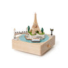 The Paris Music Box features a classic design with miniature models of the Eiffel Tower, a bridge, lamp post, trees, and a boat on a blue river.