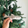 A hand displays the Finger Puppet: Shark, made of gray felt, in front of a Christmas tree with pinecones—perfect for sparking underwater-themed imaginative play.