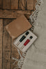An open decorative gift box featuring two Wooden Soldiers bottle stoppers, one painted black and the other red, is displayed on a wooden surface beside a fringed, light-colored rug.