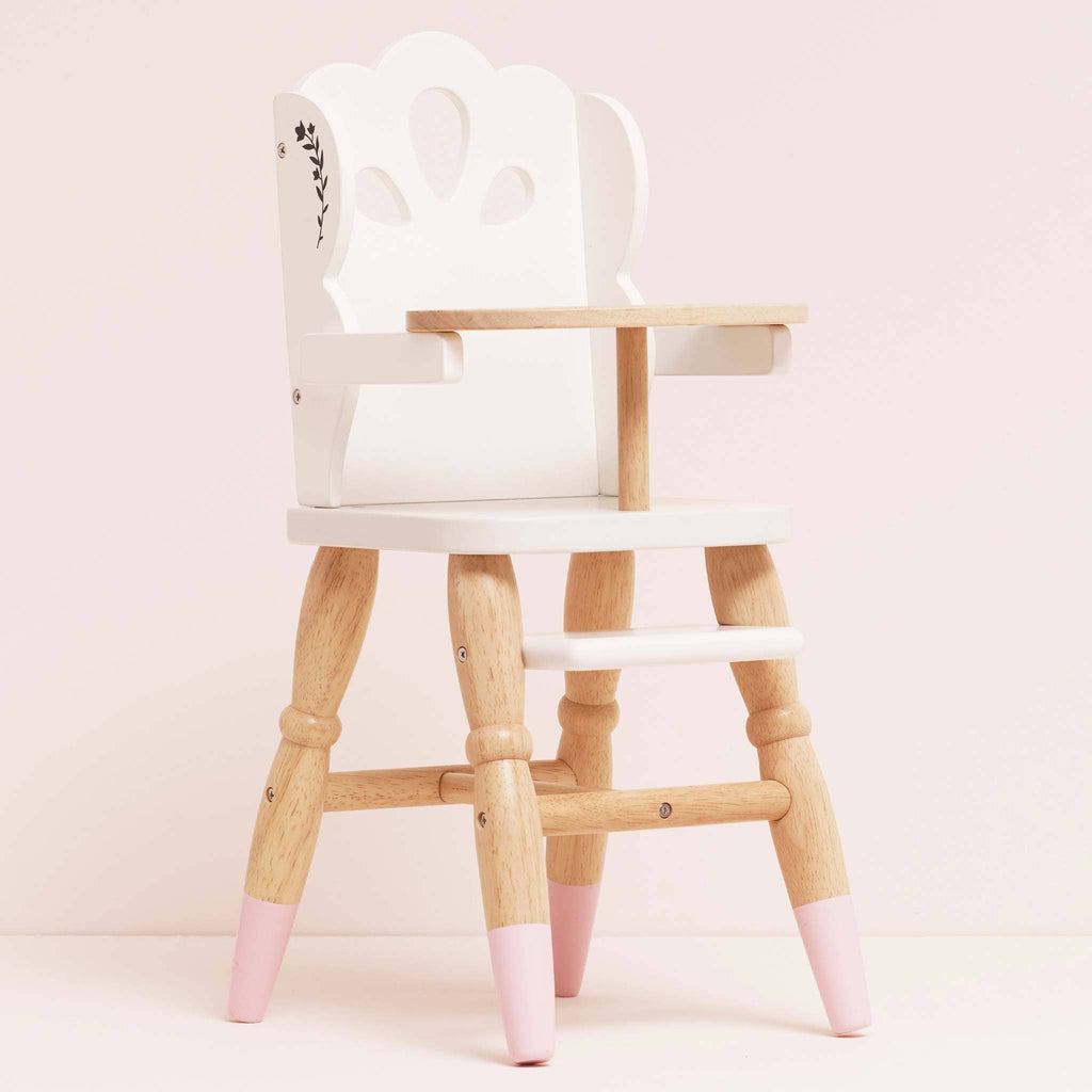 The Dolls Wooden High Chair features natural wood legs, pink-tipped feet, and a leaf design. Eco-friendly and perfect for pretend play, this charming toy is showcased against a light pink background.