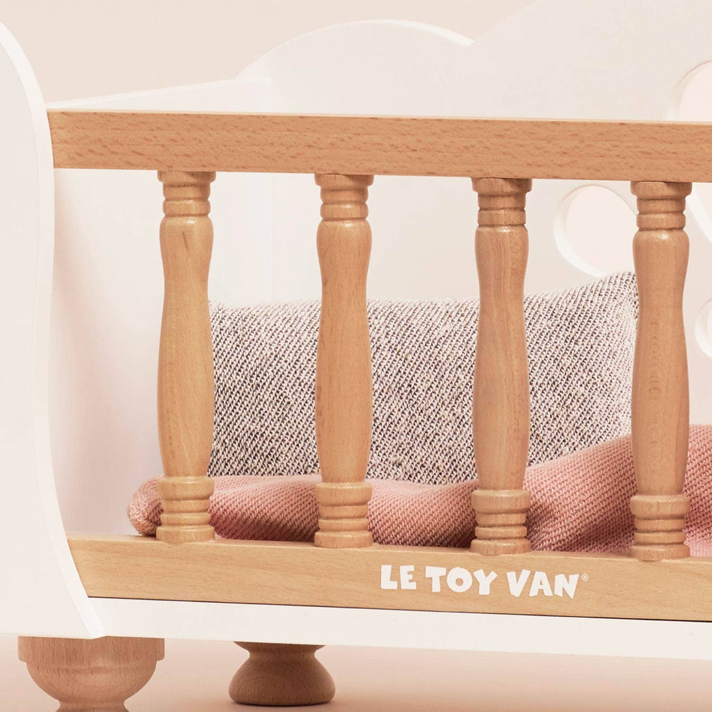 A Wooden Dolls Cot with white end panels and natural wood spindles, containing a textured gray pillow and a folded pink blanket from the soft bedding set.