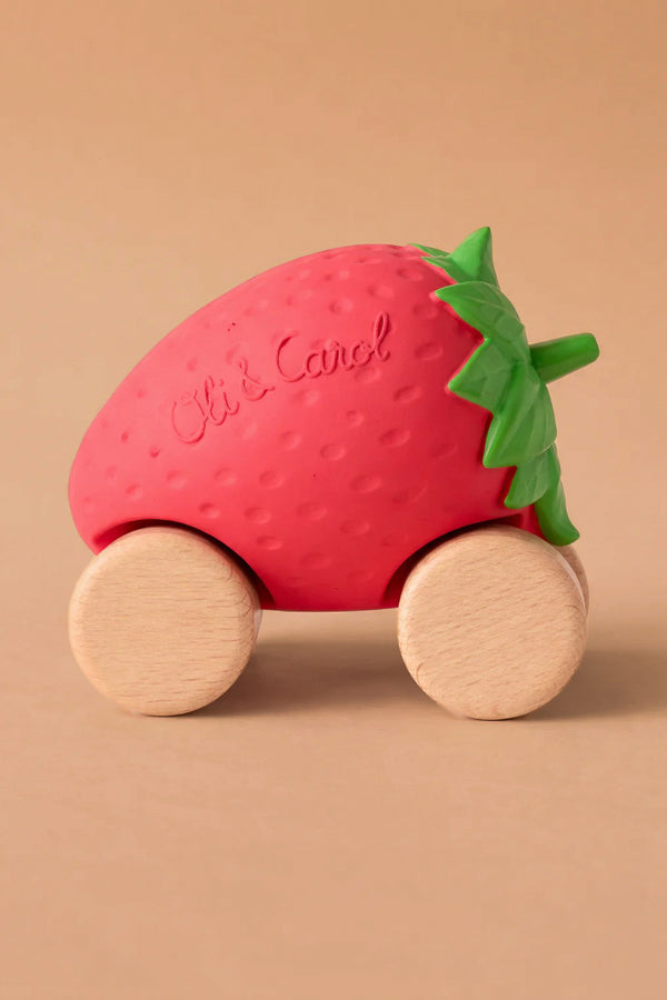 Sweetie The Strawberry Baby Car features a red strawberry shape with green leaves, mounted on four FSC-certified wood wheels. "Oli & Carol" is embossed on the strawberry, shown against a plain beige background.